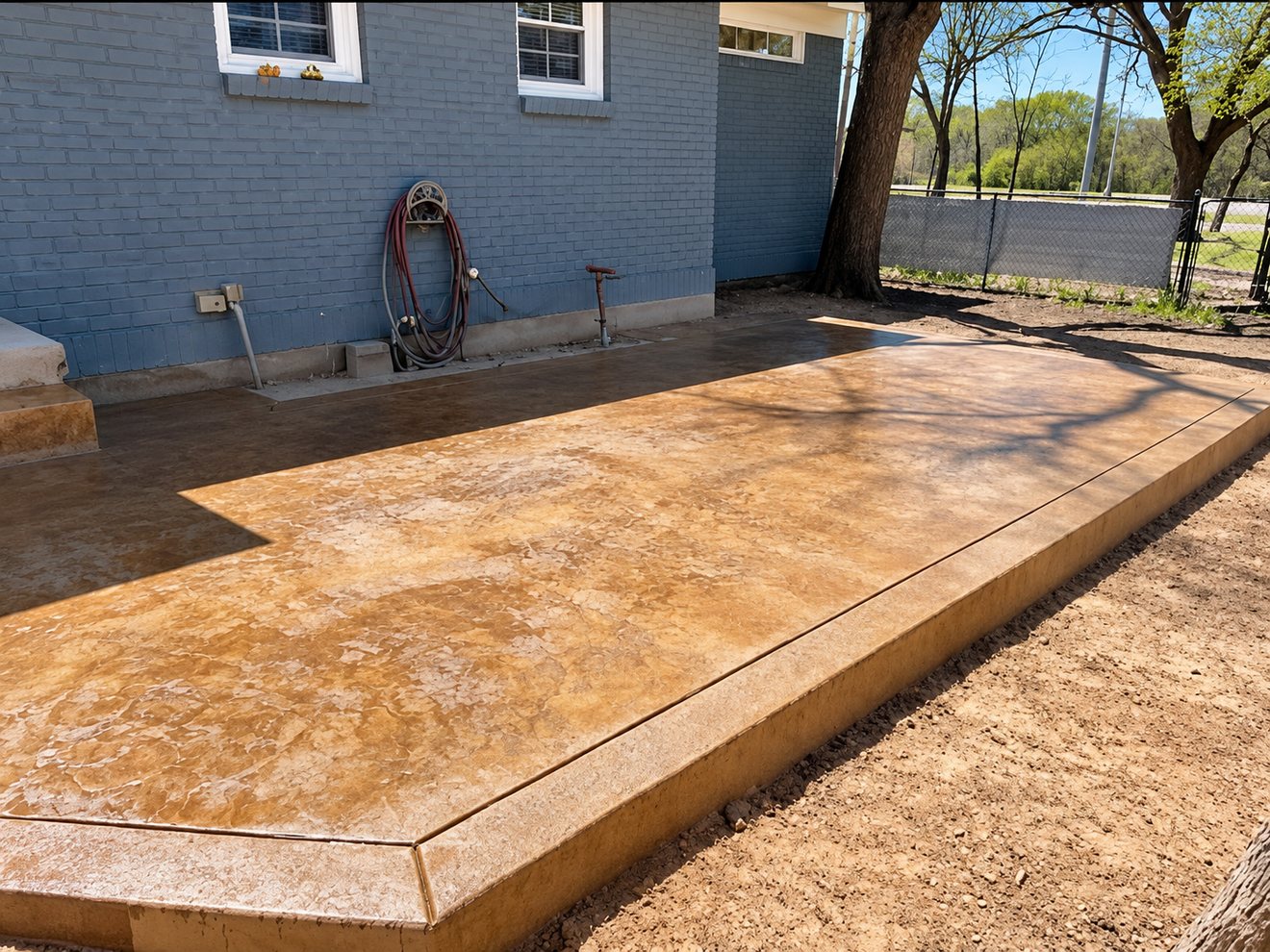 Amber stained and sealed concrete patio along a blue-painted brick house